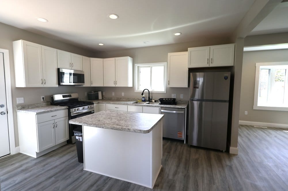 Remodeled kitchen at 2102 E Main St, Ashland WI with white shaker cabinets, center island, stainless steel appliances, and gray LVP flooring