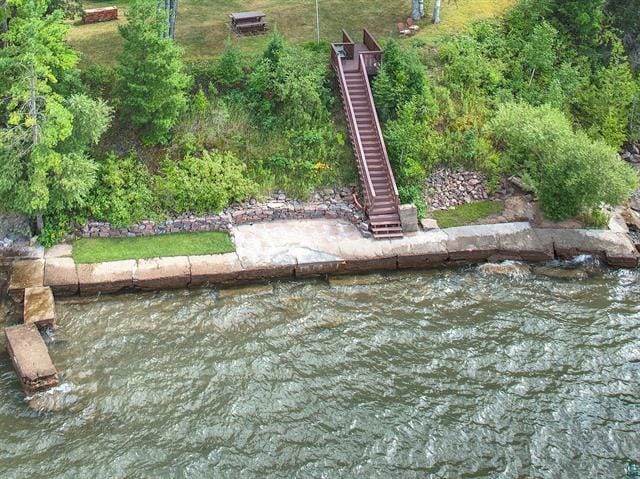 Aerial close-up of the grandfathered break wall at 55161 Corbine Rd in Ashland, WI, built from large sections of an original concrete dock laid end to end along the Lake Superior shoreline, with a walkable top surface, a concrete landing, stone riprap, and a wooden staircase descending the wooded bank.