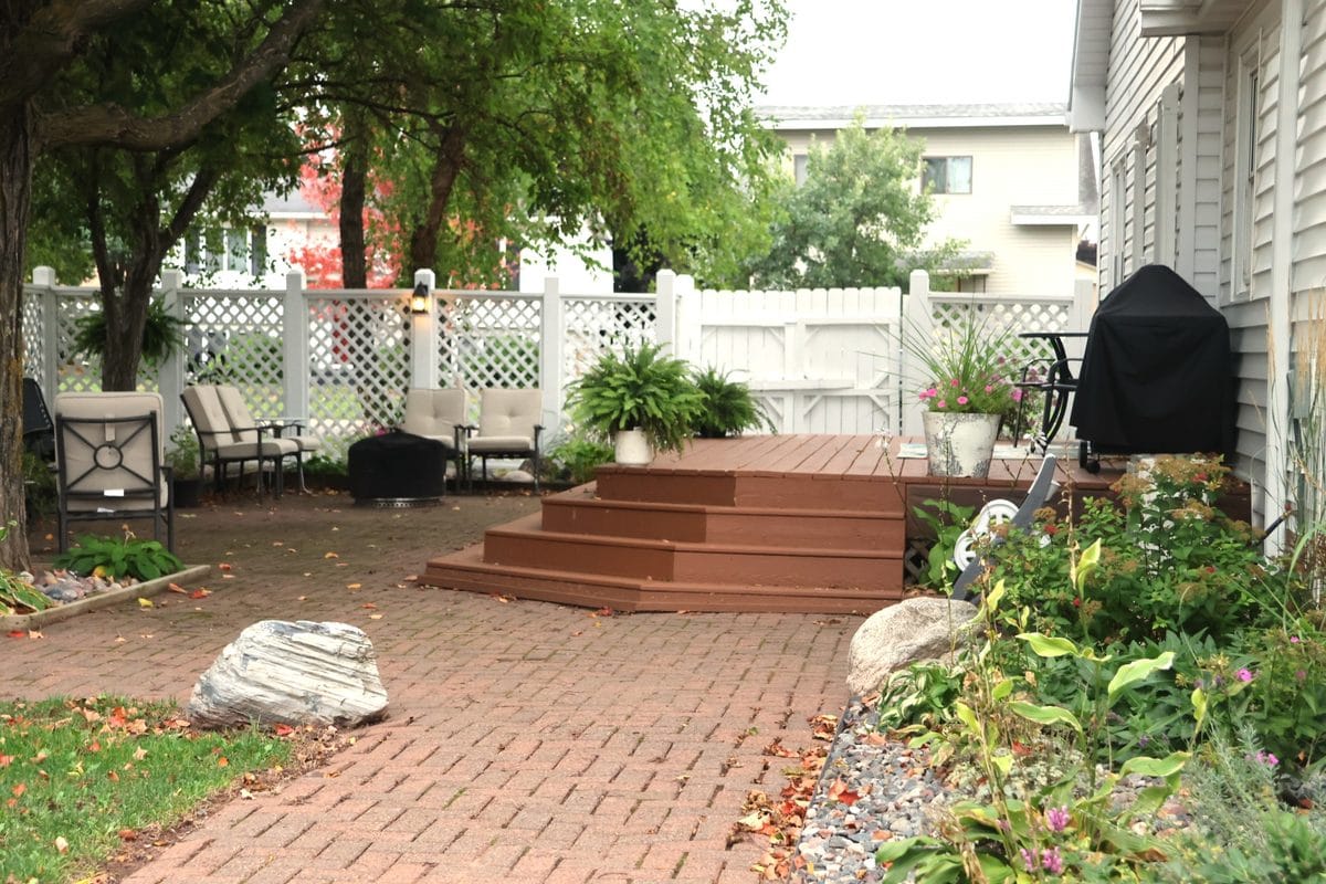 Private backyard at 914 3rd Ave E, Ashland WI with two-tier deck, brick paver patio, outdoor seating area, perennial gardens, and white privacy fencing