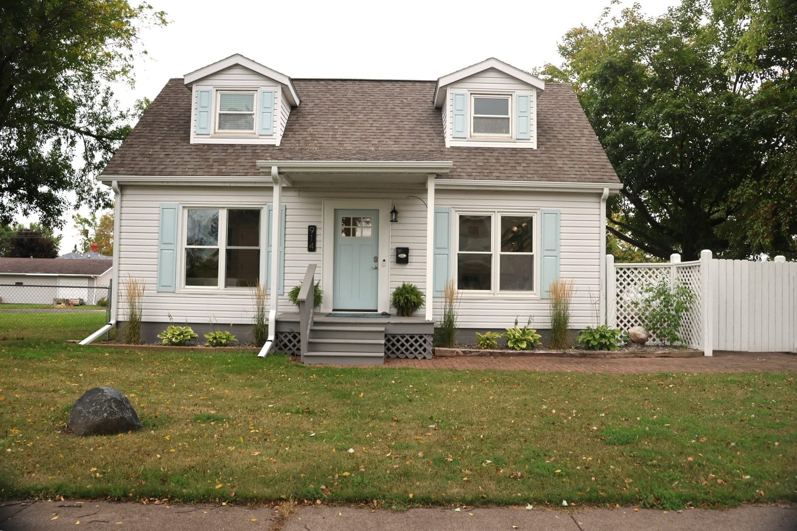 914 3rd Ave E, Ashland WI - remodeled 1.5-story home for sale with twin dormers, light blue shutters and front door, covered entry, and landscaped front yard