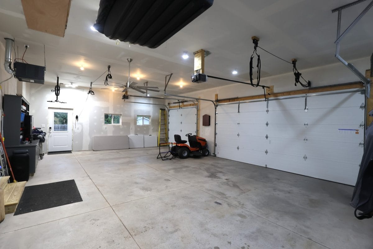 New 2025 heated and insulated 3-car attached garage at 914 3rd Ave E, Ashland WI with ceiling-mounted heater, ceiling fan, overhead storage, service door, and two overhead garage doors