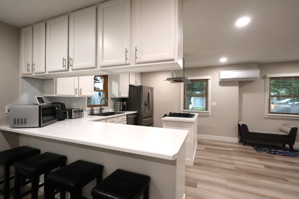 Remodeled kitchen at 914 3rd Ave E, Ashland WI with white cabinets, breakfast bar with seating, island with gas cooktop and stainless range hood, stainless steel appliances, and light LVP flooring